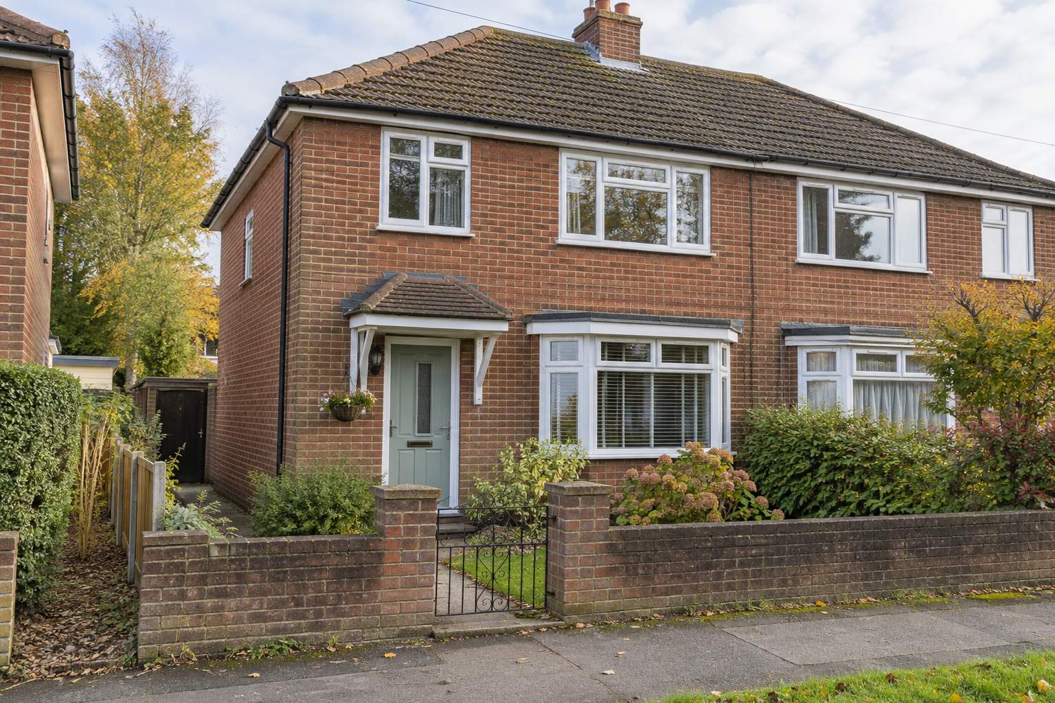Red-brick semi-detached home with white replacement windows and a planted front garden